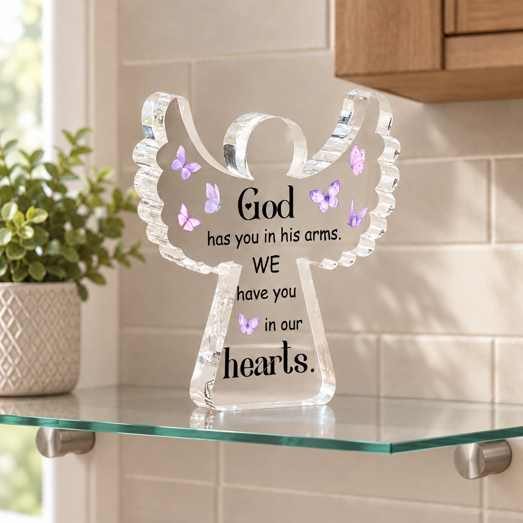 Angel-shaped acrylic memorial keepsake on a glass floating shelf in a light kitchen corner; shelf and plant not included